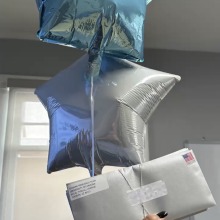 A hand holds up study kits along with two star-shaped light blue balloons.