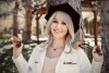 A woman wears a doctor's coat and doctoral tam and smiles.